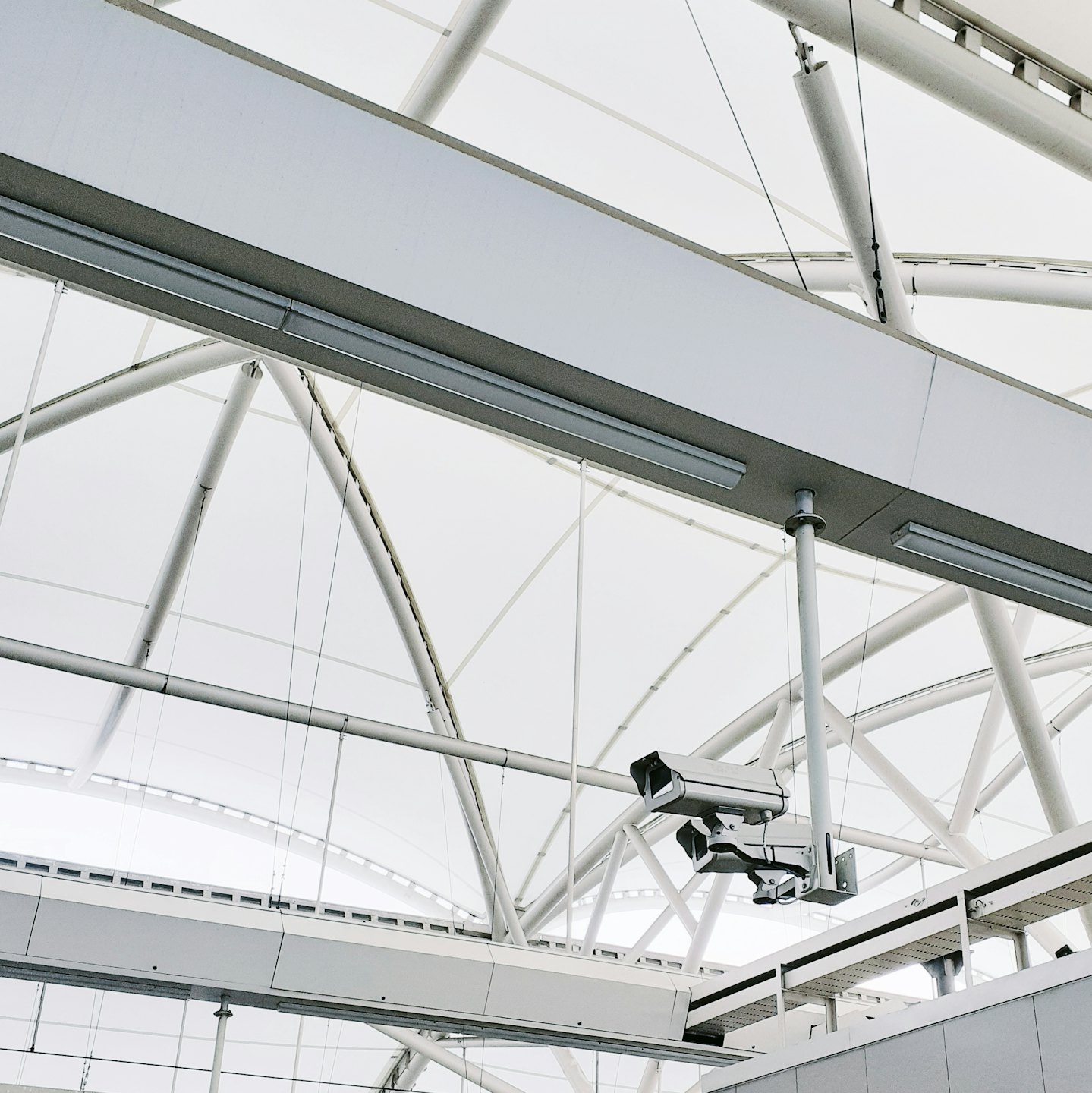 White tensile ceiling with grey beams and security cameras.